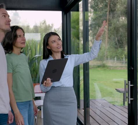 Beautiful Latin American Real Estate Agent holding a tablet while showing the view to customer couple looking at a property - Home ownership concepts